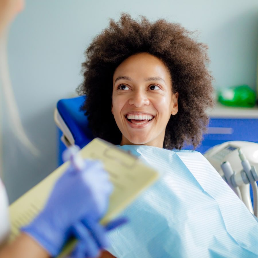 A woman sits in a clinic chair while speaking with the dentist