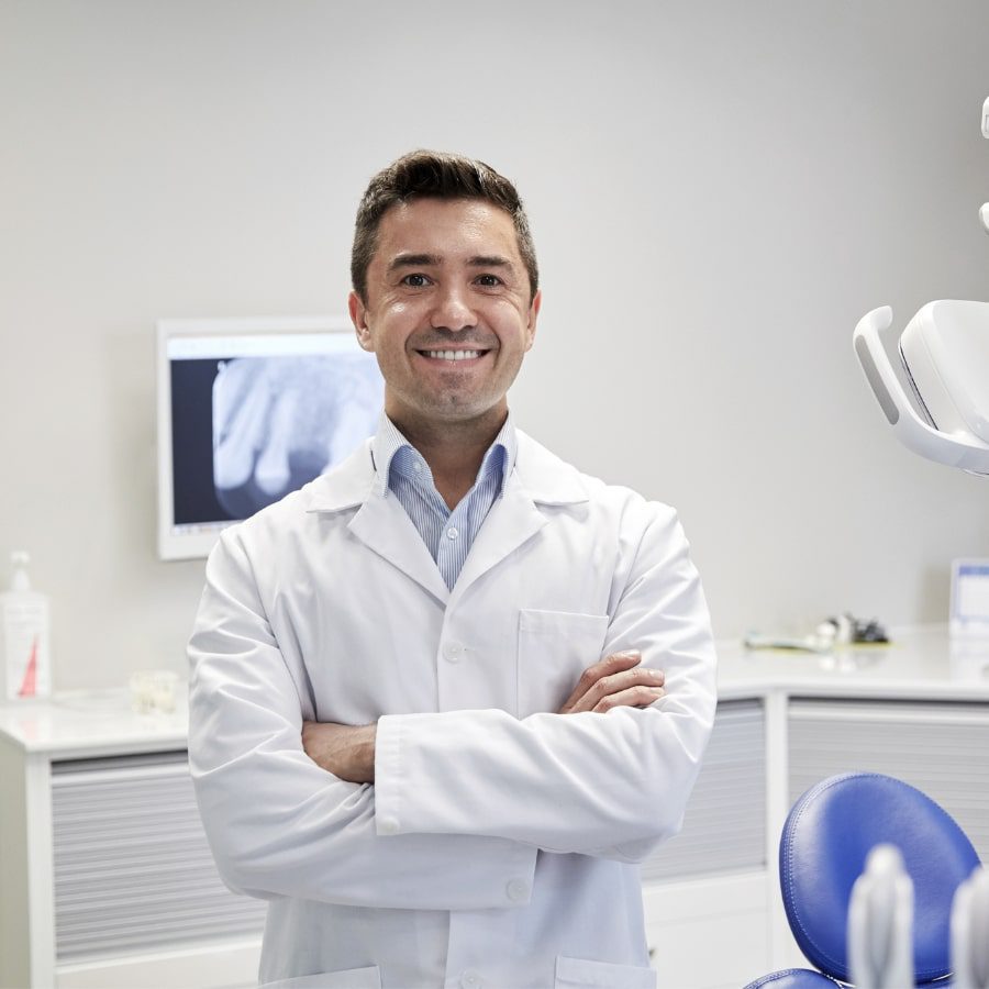 A dentist stands in his clinic smiling at the camera