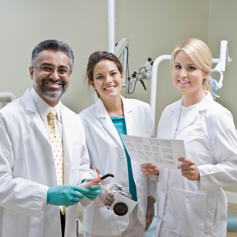 Three dentists stand in a clinic smiling