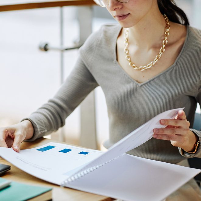 A woman sits at a desk and flips through a notebook containing graphs